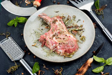 Çiğ pirzola, Tomahawk, baharatlı otlar içinde terbiye edilmiş taştan arka planda.