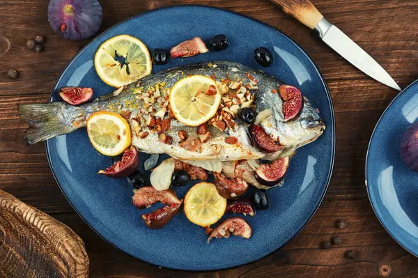 Roasted dorado fish with almonds and figs on rustic wooden table. Autumn recipe. Top view.