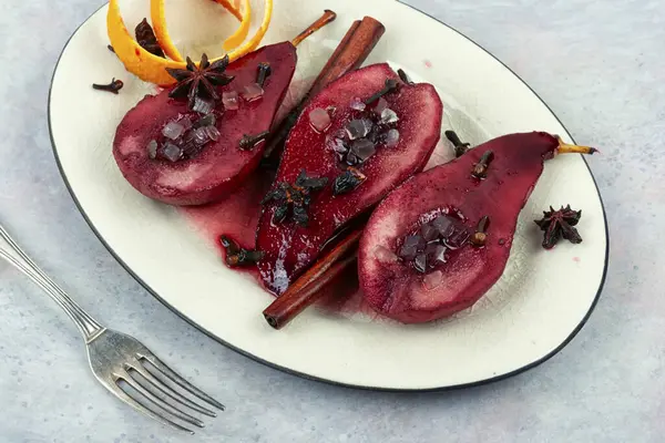 Poached autumn pears in red wine and candied fruits on the white plate. Caramelized pears.