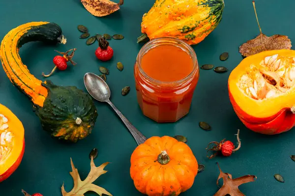 Autumn sweet pumpkin jam in a glass jar and fresh pumpkins. Pumpkin confiture.
