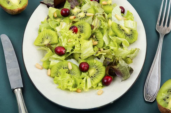 Raw salad of kiwi, lettuce, berries and pine nuts in old ceramic plate . Keto diet, salad plate.