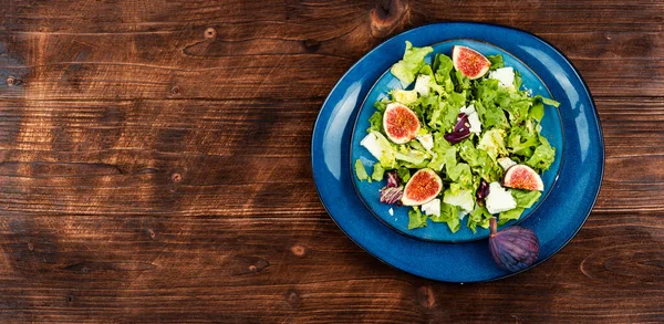 Raw dieting salad with figs, herbs and cheese on old wooden background. Copy space