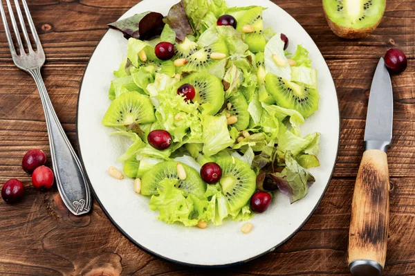Vitamin salad of kiwi, greens, berries and pine nuts on wooden table. Clean eating.