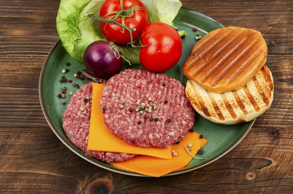 Raw burger patties, cheese, vegetables and burger buns for cooking. Raw hamburgers.