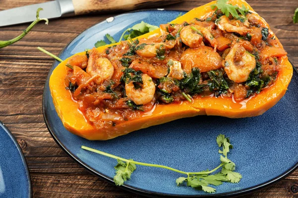 Half a butternut squash stuffed with vegetables and shrimp on wooden table.