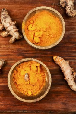 Ahşap arka planda ham zerdeçal kökü ve zerdeçal tozu..