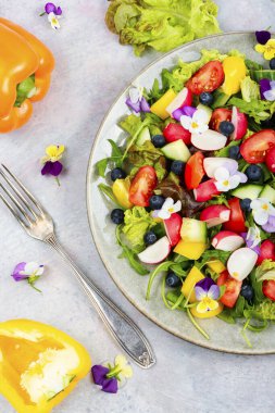 Yenilebilir çiçeklerle süslenmiş taze sebze salatası. Üst görünüm.