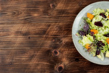 Sonbahar vejetaryen salatası, kavrulmuş balkabağı, pancar ve kırsal ahşap arka planda yeşillikler. Metin için boşluk olan üst görünüm.