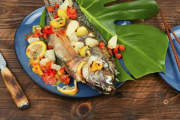 Fried tilapia fish with citrus sauce on leaf background.