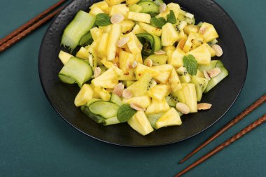 Vegan taze ananas ve salatalık salatası. Siyah tabakta ve çubukta servis edilen ananas salatası..