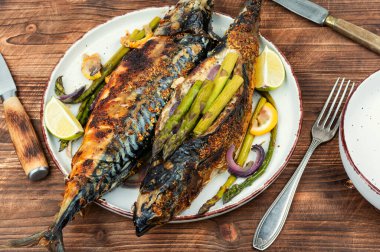 Kırsal ahşap masada yeşil kuşkonmazla pişirilmiş iki uskumru balığı.