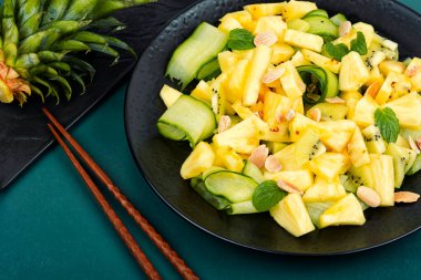 Siyah tabakta servis edilen salatalıklı taze ananas salatası. Vejetaryen ananas salatası ve çubuk.