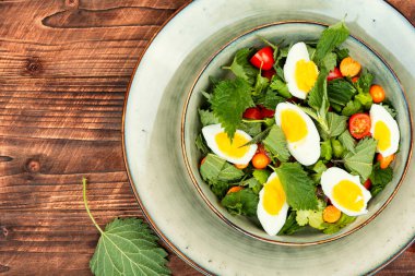 Isırgan otlu yeşil salata, domates ve eski ahşap arka planda yumurtalar. Ukrayna yemekleri.