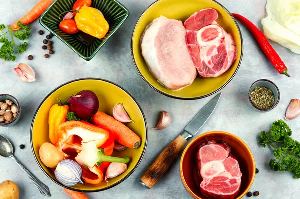 stock image Fresh meat and vegetables on the kitchen table. Raw beef bones and pork for soup. Top view, flat lay.