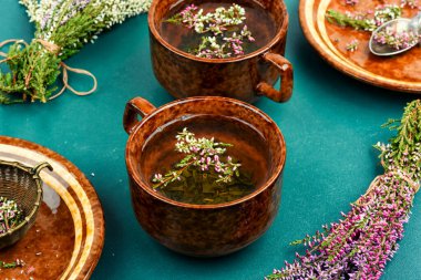 Heather herbal tea in a mug and forest herbs on a table. clipart