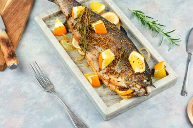 Portakal sosunda pişmiş iştah açıcı alabalık ve şık bir taş servis tahtasında biberiye..