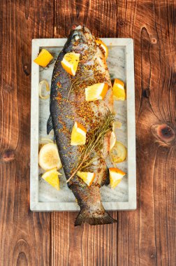 Ahşap arka planda turuncu taştan bir tabakta tam pişmiş alabalık..