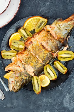 Bir tabak tam pişmiş alabalık, kivi ve portakalla servis ediliyor..