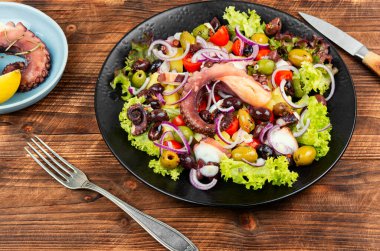 Ahtapot dokunaçları, zeytin ve patates tabağı. Ahtapot salatası ahşap bir masada..