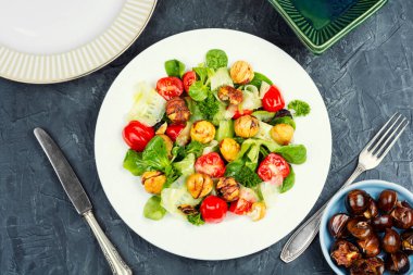 Beton mutfak masasında kızarmış kestane, taze domates, salatalık ve yeşillik ile vejetaryen salatası. Üst görünüm.