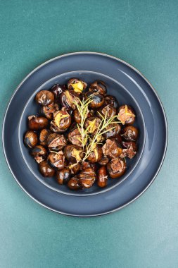 Kavrulmuş kestaneler, kavrulmuş kestaneler... Bazı kestaneler çatlamış, taze biberiye ile süslenmiş, sonbahar yapraklarıyla şekillendirilmiş. Üst görünüm.