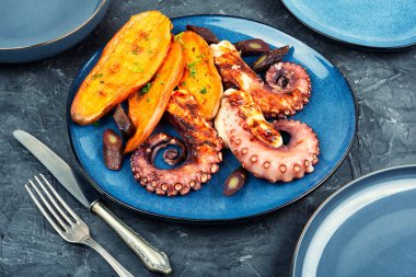 Fırında pişmiş patates dilimleriyle süslenmiş ızgara ahtapot dokunaçları. Yemek fotoğrafçılığı.
