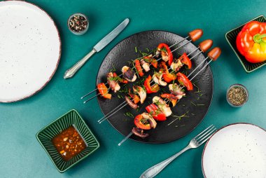 Dolmalık biberle süslenmiş ızgara ahtapot şişleri. Siyah tabakta deniz mahsulleri..