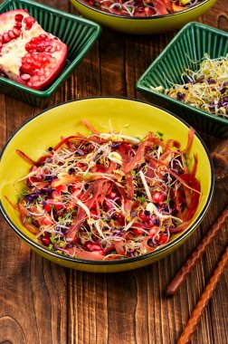 Salad of sprouted alfalfa, beans, red radish with pomegranate seeds and black carrots on wooden rustic background. clipart