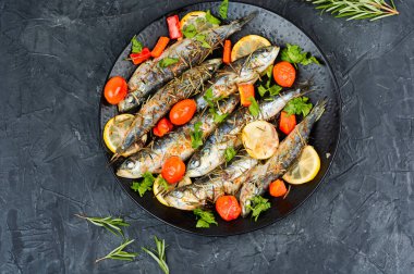 Limonlu fırında sardalya balığı, seramik tabakta kirazlı domates ve biberiye. Sağlıklı bir akşam yemeği. Üst görünüm.