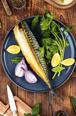 Whole smoked mackerel on a plate with greens, lime and spices. Rustic style. clipart