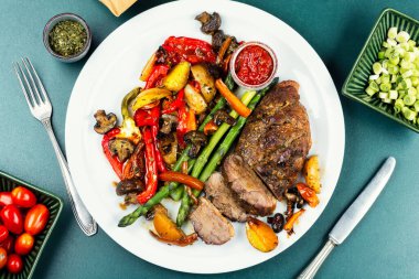 Bir tabak kızarmış ördek göğsü eti, fırında sebze, kuşkonmaz ve ızgara et. Düz yatıyordu