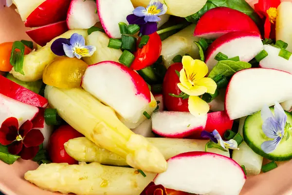 Yenilebilir çiçeklerle süslenmiş beyaz kuşkonmazlı sebze salatası. Vejetaryen mutfağı, yemek geçmişi.