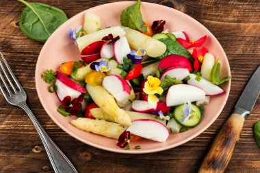 Bahar salatası, beyaz kuşkonmazlı yeşil salata ve tahta yüzeyde yenilebilir çiçekler..