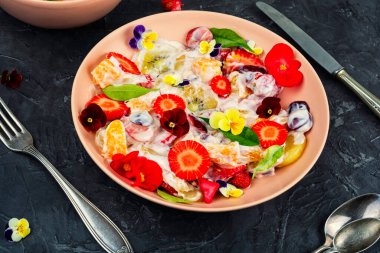Bir tabak meyve salatası, sağlıklı organik meyve salatası, beyaz yoğurt ve yenilebilir çiçeklerle süslenmiş..