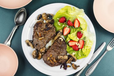 Aromatik kavrulmuş dana eti ve bir garnitür taze çilek ve marul ile biftek. Düz yatıyordu.