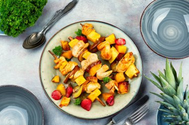 Kızarmış tavuk parçaları ve bir tabakta ananas, meyve ve et şişleri. Düz yatıyordu.