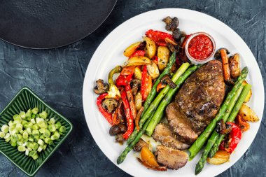 Bir tabak kızarmış ördek göğsü eti, fırında sebze, kuşkonmaz ve ızgara et. Düz yatıyordu