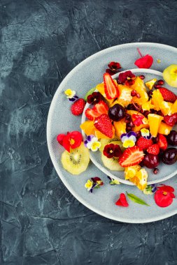 Taze meyve dolu kâse ya da tabak, lezzetli karışık meyve salatası yenebilir çiçekler..