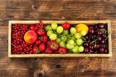 Olgun meyve ve meyvelerin, üzümlerin, üzümlerin, üzümlerin, üzümlerin, çileklerin ve kayısıların ahşap arka planda canlı çeşitleri..