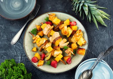 Kızarmış tavuk parçaları ve bir tabakta ananas, meyve ve et şişleri. Düz yatıyordu.