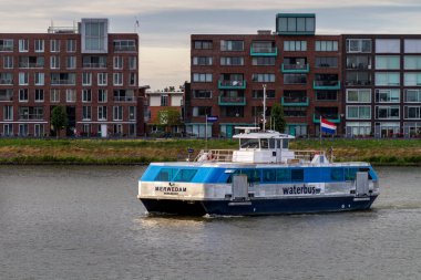 Dordrecht, Netherlands - July 17, 2015: Dutch Waterbus sails between Dordrecht and Papendrecht. The shimmering water of the Beneden Merwede river reflects the warm hues, creating a tranquil scene. clipart