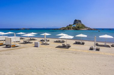 Yunanistan 'ın Kos adasındaki cennet adasının önündeki güzel Agios Stefanos Sahili' nin güverte sandalyesi ve şemsiyesi.