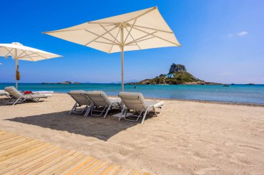 Yunanistan 'ın Kos adasındaki cennet adasının önündeki güzel Agios Stefanos Sahili' nin güverte sandalyesi ve şemsiyesi.