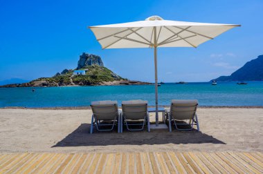 Yunanistan 'ın Kos adasındaki cennet adasının önündeki güzel Agios Stefanos Sahili' nin güverte sandalyesi ve şemsiyesi.