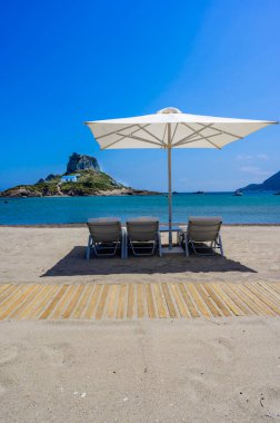 Yunanistan 'ın Kos adasındaki cennet adasının önündeki güzel Agios Stefanos Sahili' nin güverte sandalyesi ve şemsiyesi.