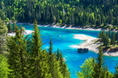 Small island in the middle of Cauma Lake (Caumasee) with crystal blue water in beautiful mountain landscape scenery at Flims, Graubuenden - Switzerland