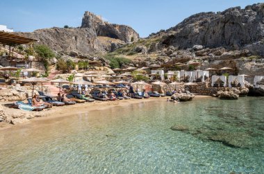 Lindos, Yunanistan - 24 Mayıs 2023: St. Paul 's Pembe Plajı Sahil Sandalyeleri ve Kulübeleri ve Akdeniz Güneşi Altında Rahatlayan Turistler