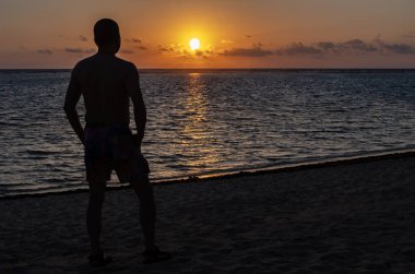Tropik bir plajda güzel bir güneşin doğuşuna bakan bir adamın silueti.