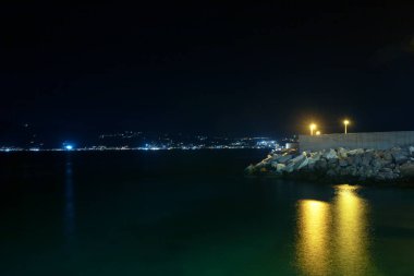 Photograph of the coast of Villa San Giovanni, in Reggio Calabria, at night and the island of Sicily. Long exposure photography, silk effect in sea water