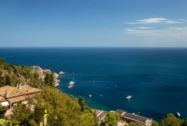 Photograph of the coast of Taormina, on the island of Sicily, during the summer afternoon, houses and trees, boats and the Mediterranean se